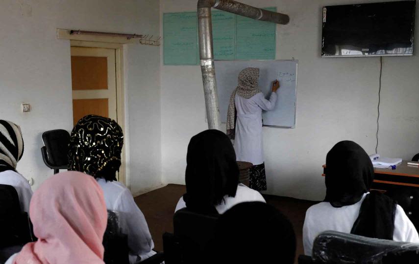 A teacher in a small classroom is writing on a whiteboard as she gives a lecture to trainee midwives in Bamiyan, Afghanistan, on 2 March 2023, part of an initiative spearheaded by the UN's refugee agency (UNHCR) in partnership with a local NGO.