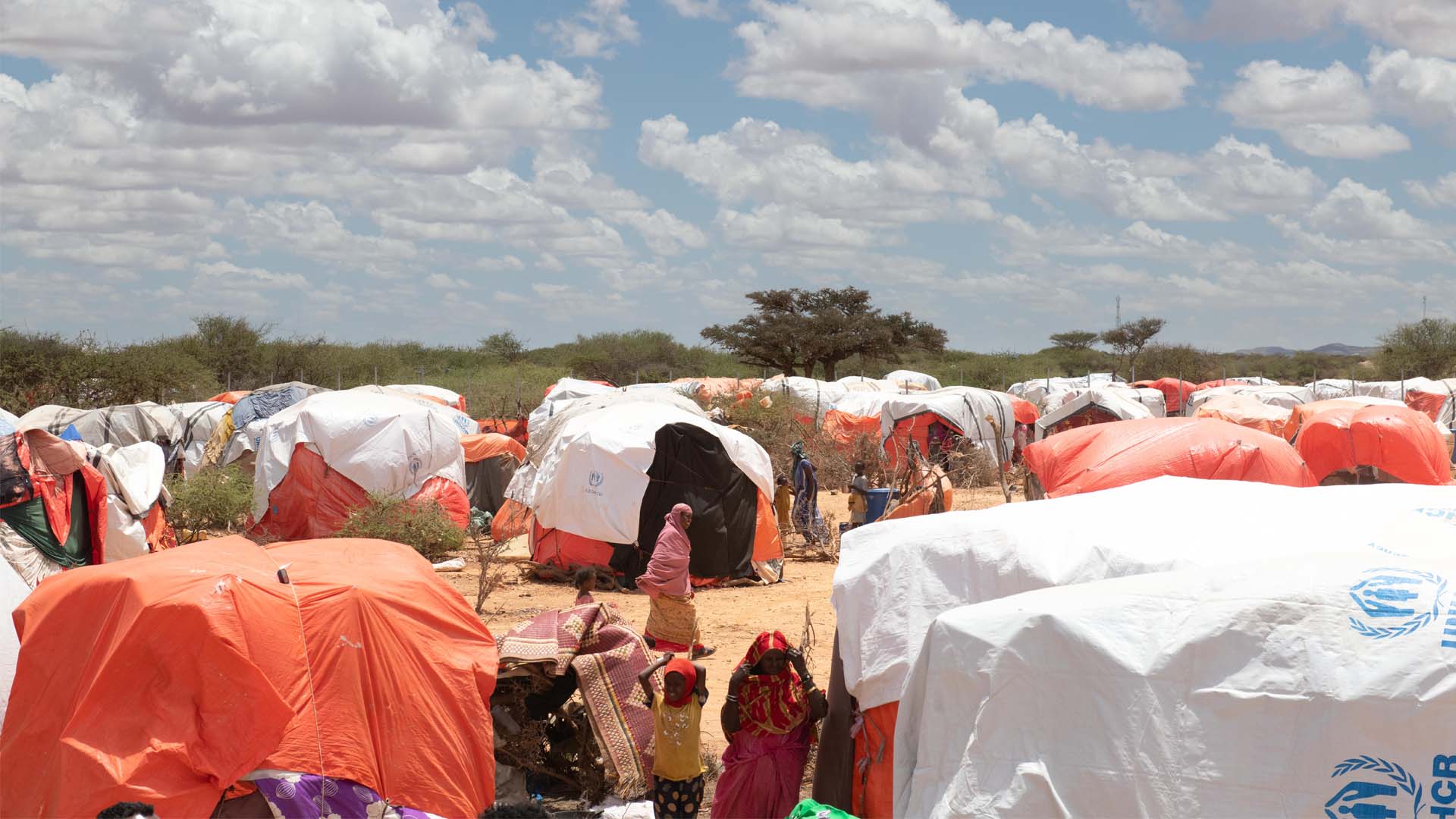 A woman is pictured at a distance walking in between encampments. These are temporary tent shelters in an informal refugee camps outside Kalabaydh, Somalia.