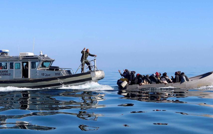 This picture shows Tunisian coast guards try to stop migrants at sea during their attempt to cross to Italy, off the coast off Sfax, Tunisia April 27, 2023. The Tunisian coast guard boat is to the left, the migrant boat is to the right. A man stands at the front of the coast guard boat and is seen speaking to the migrants on the migrant boat.