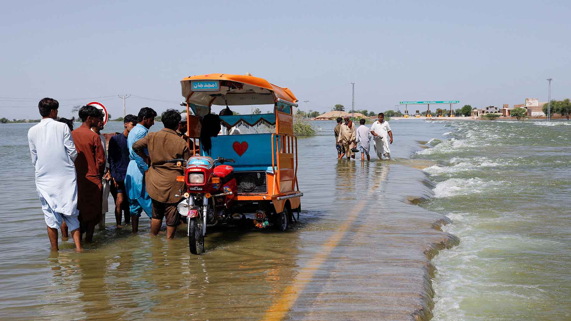 Displaced people stand next to a Tuktuk on flooded highway, following rains and floods during the monsoon season in Sehwan, Pakistan, September 16, 2022.