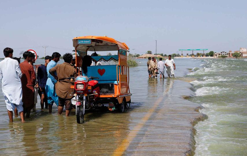 Displaced people stand next to a Tuktuk on flooded highway, following rains and floods during the monsoon season in Sehwan, Pakistan, September 16, 2022.