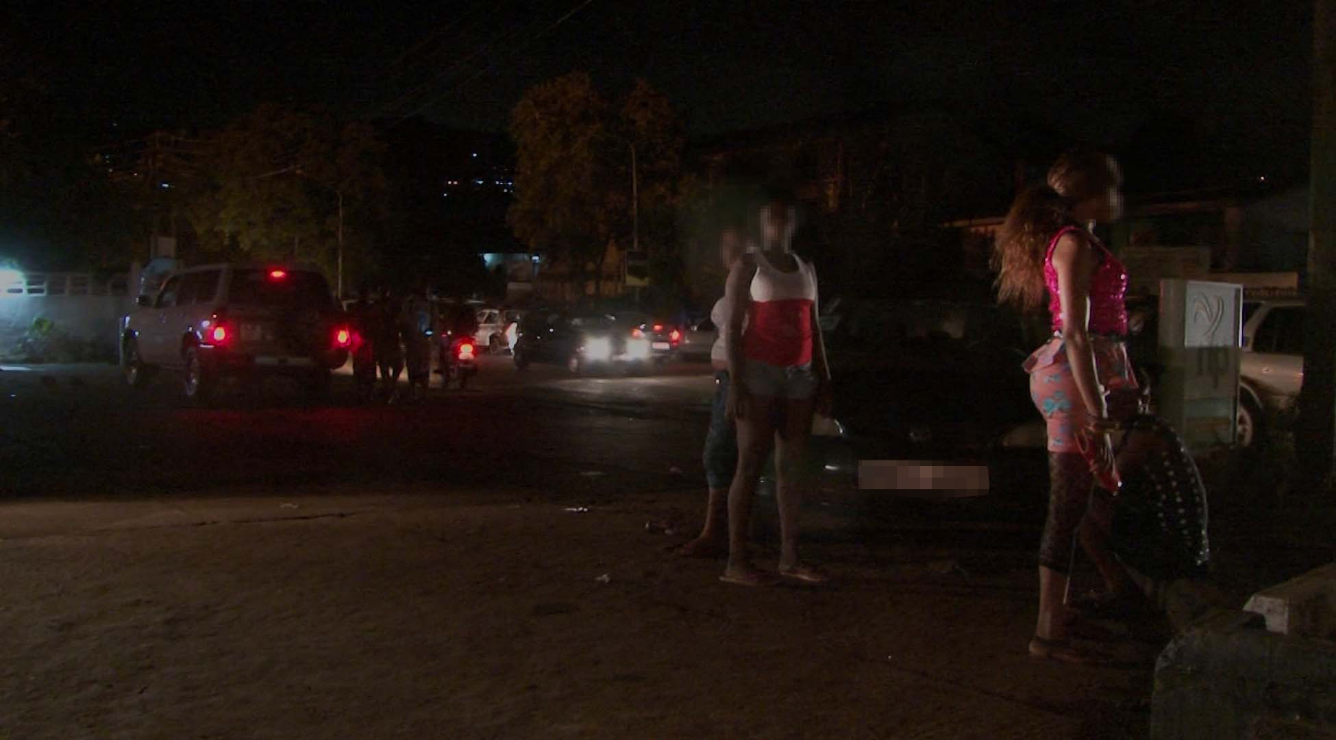 Three women stand to the side of a street at night.