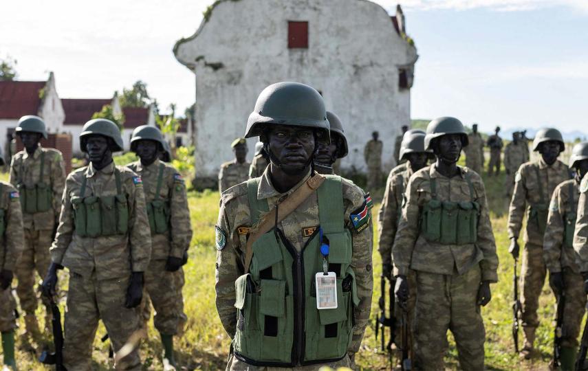 This is a photograph that shows rows of members of the South Sudanese army, part of the troops to the East Africa Community Regional Force (EACRF). At the center of the frame is one man looking directly into the camera, his right eye seems to have been injured.