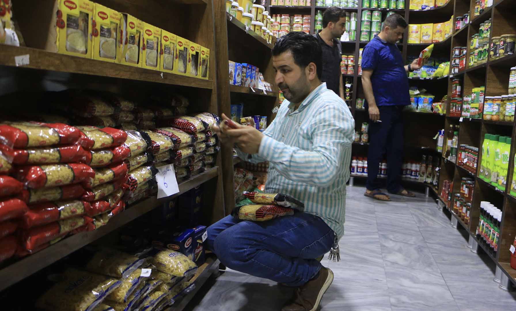  The owner of a small supermarket in Idlib, northwest Syria, is crouched next to shelves in a convenience store and checks the rising price tags on the goods he sells.