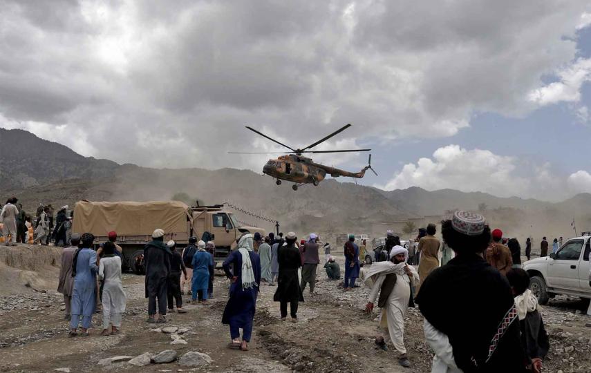 A wideshot of a Taliban helicopter carrying aid above a crowd of people. It is landing in an earthquake affected area in Gayan, Afghanistan, June 23, 2022.